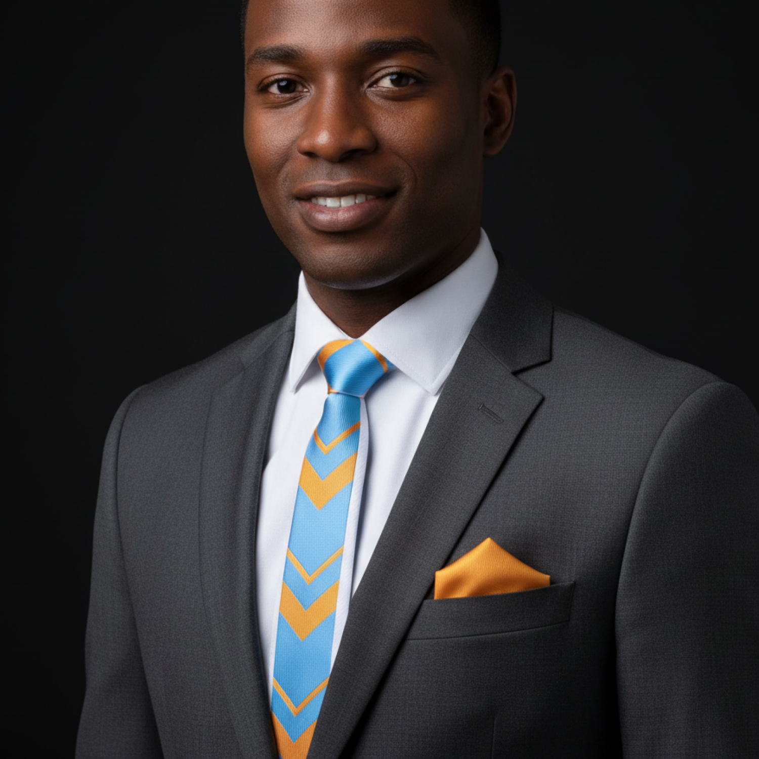 Man wearing a gray suit with a blue tie featuring yellow chevrons and an orange pocket square on a black background.