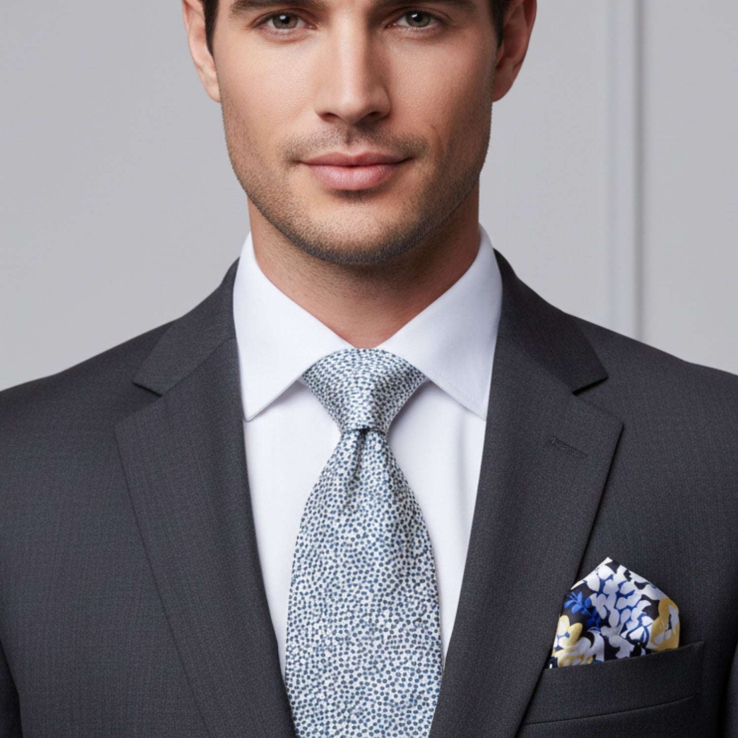 Man wearing a gray suit with a patterned tie and pocket square against a neutral background