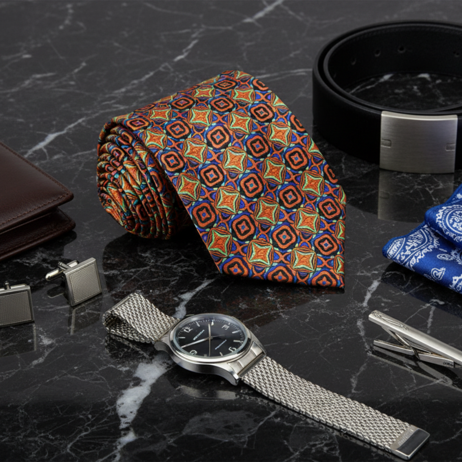 Colorful patterned tie, silver watch, cufflinks, and belt on a dark marble surface