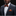 Man wearing a gray suit with an orange polka dot bow tie and pocket square on a black background