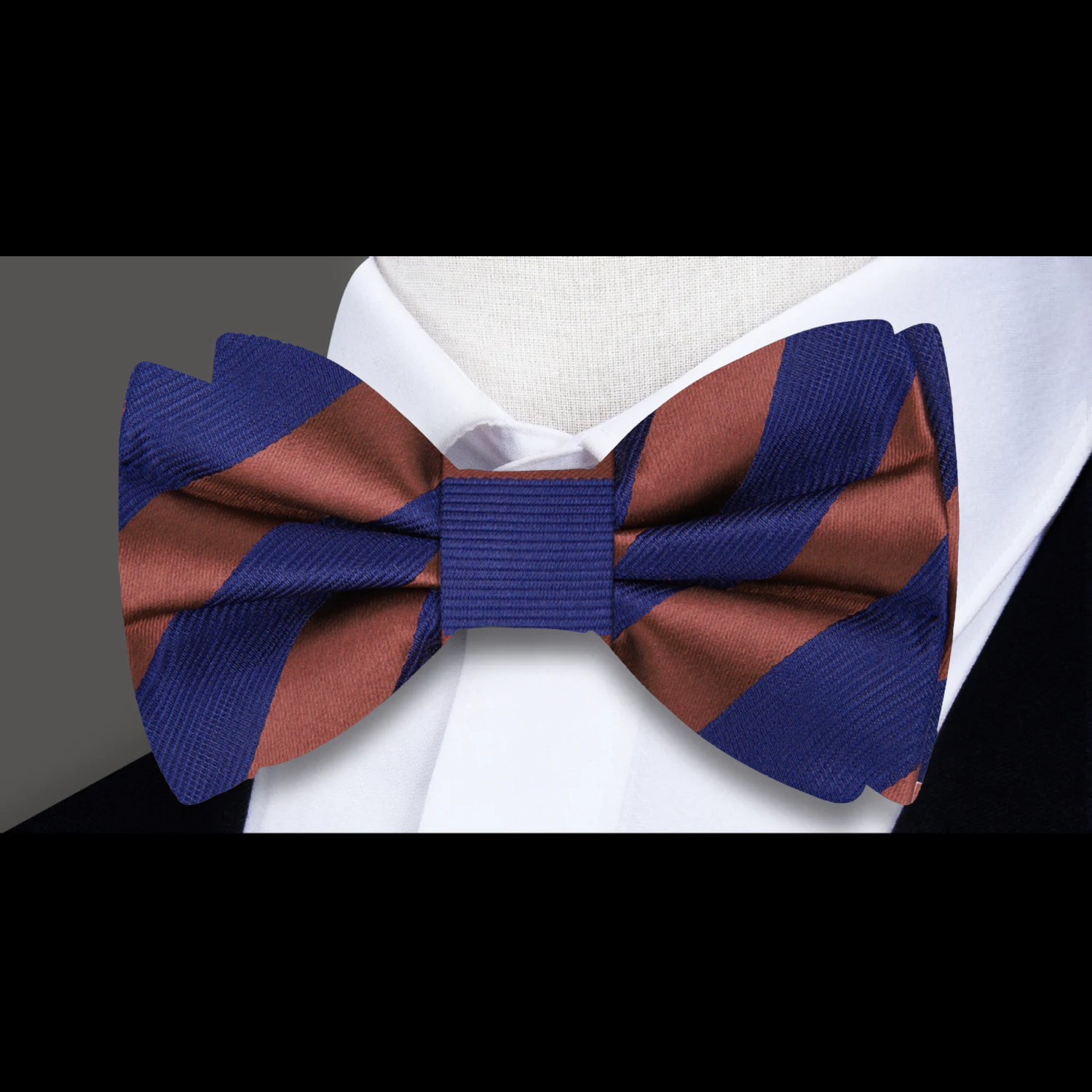 A bow tie with brownish orange and blue block stripes placed on a wooden surface with green leaves in the background.