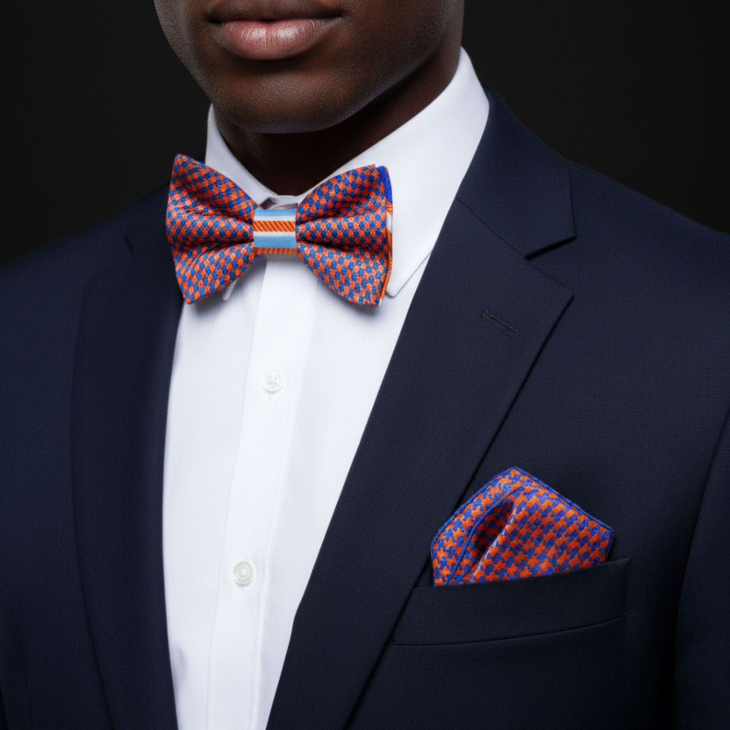 Man wearing a navy suit with a colorful bow tie and pocket square against a black background
