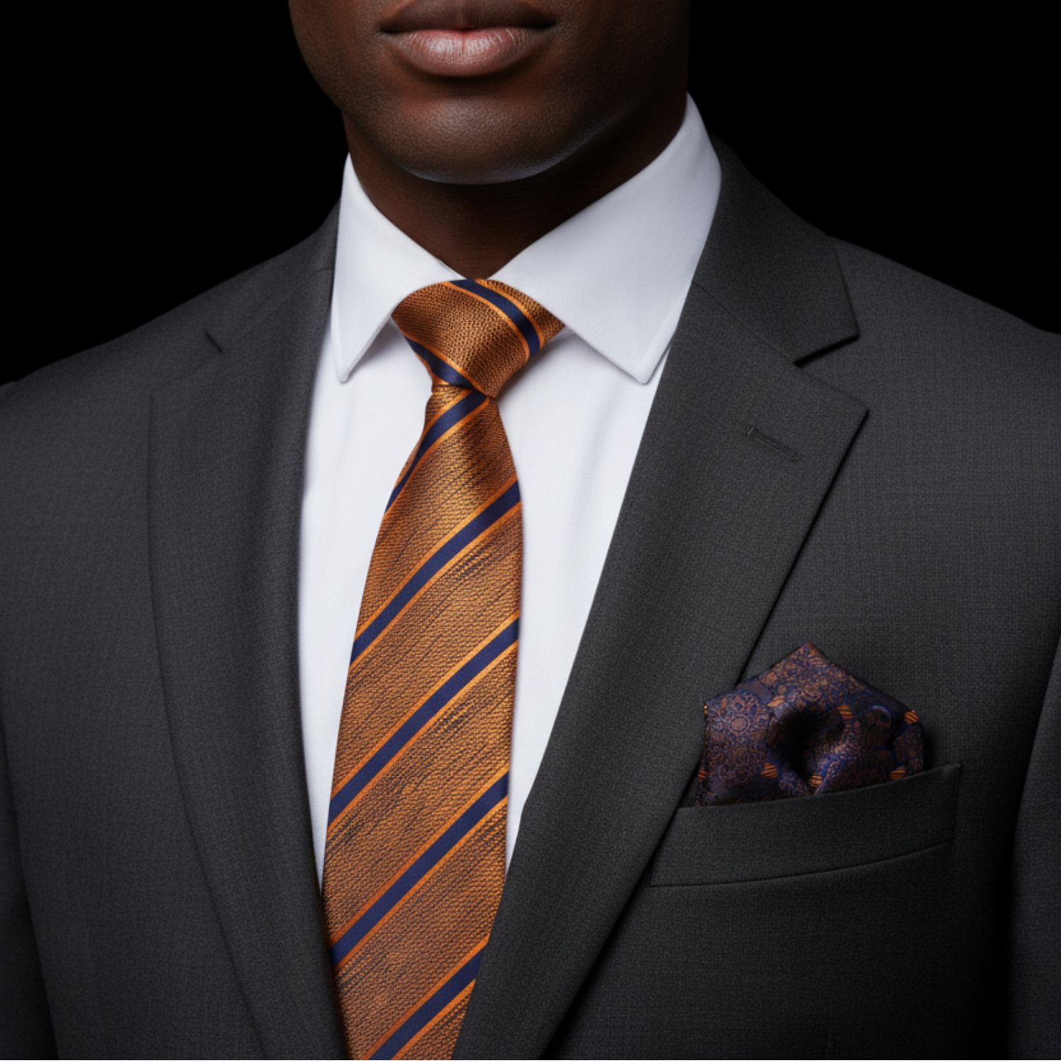 Man wearing a gray suit with a brown striped tie and pocket square on a black background