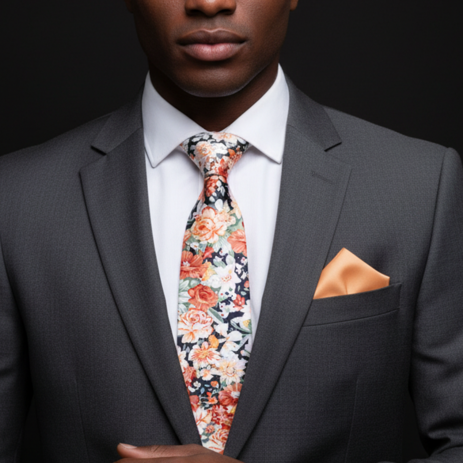 Man wearing a gray suit with a floral tie and orange pocket square on a black background