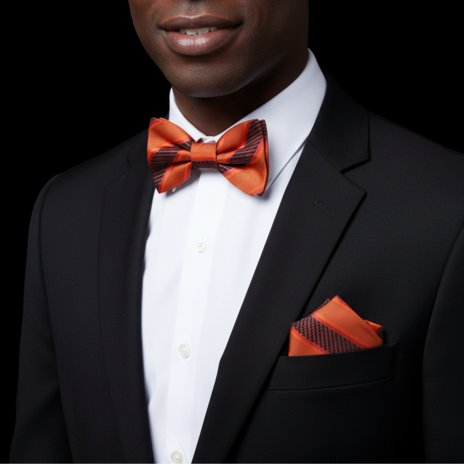 Man wearing a black suit with an orange bow tie and pocket square on a black background