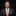 Man wearing a dark suit with an orange tie and pocket square on a black background