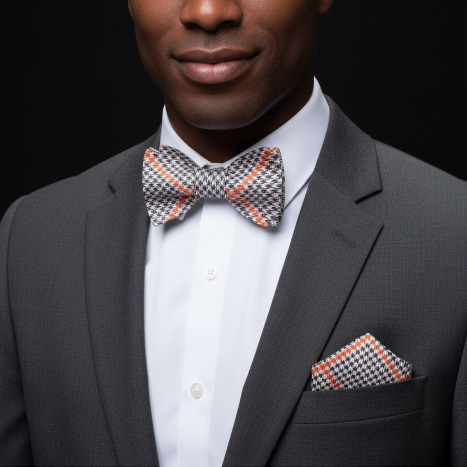 Man wearing a gray suit with a patterned bow tie and pocket square on a black background