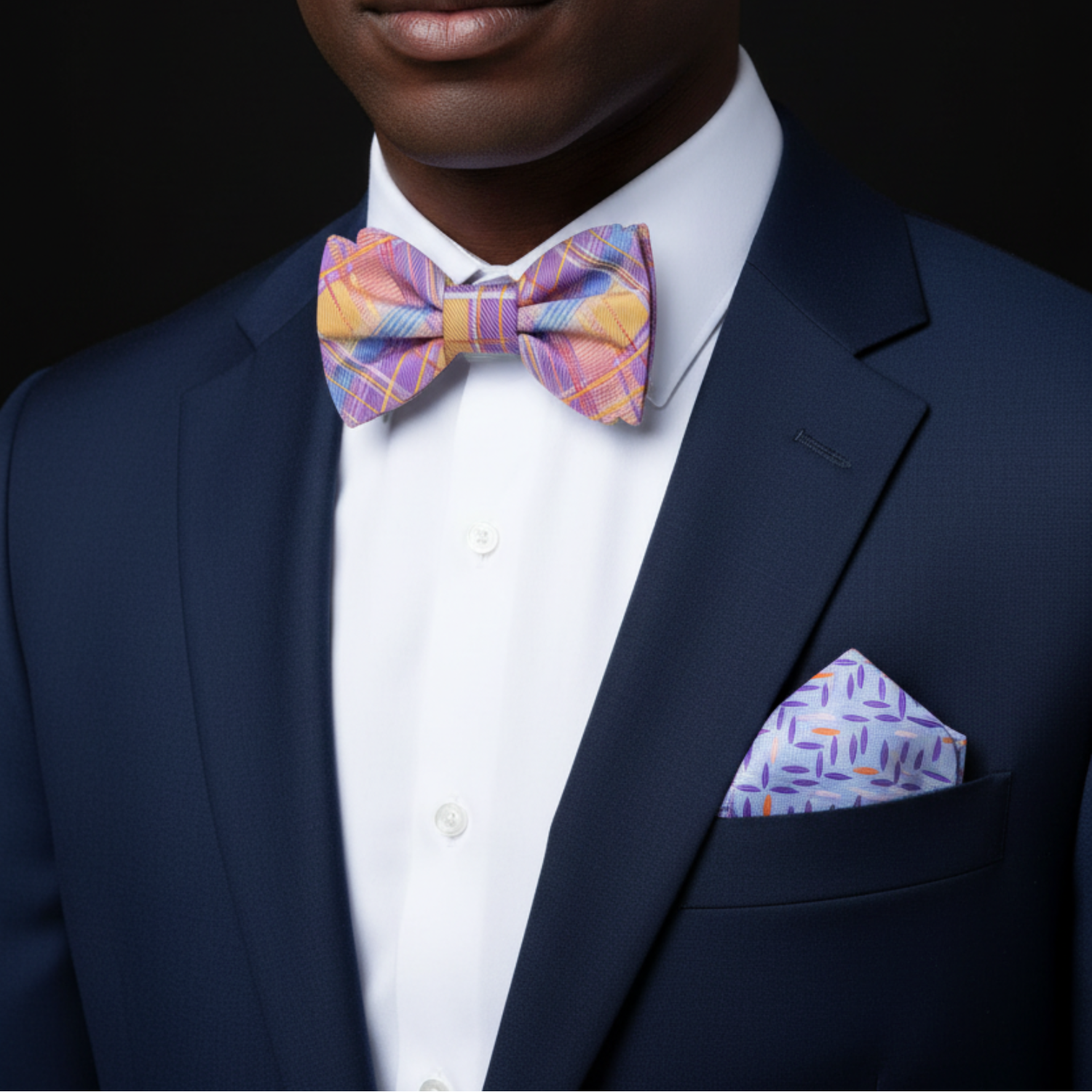 Man wearing a navy suit with a colorful bow tie and pocket square against a black background