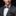 Man wearing a gray suit with a colorful bow tie and patterned pocket square on a black background