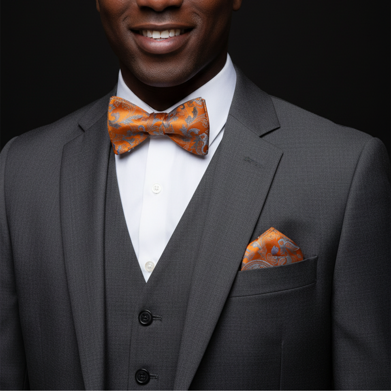 Man wearing a gray suit with an orange bow tie and pocket square on a black background