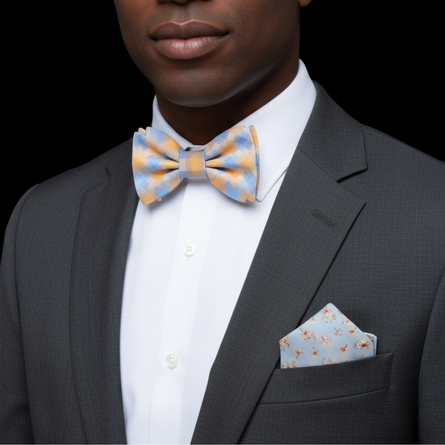 Man wearing a gray suit with a patterned bow tie and pocket square on a black background