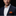 Man wearing a navy suit with an orange patterned pocket square against a black background