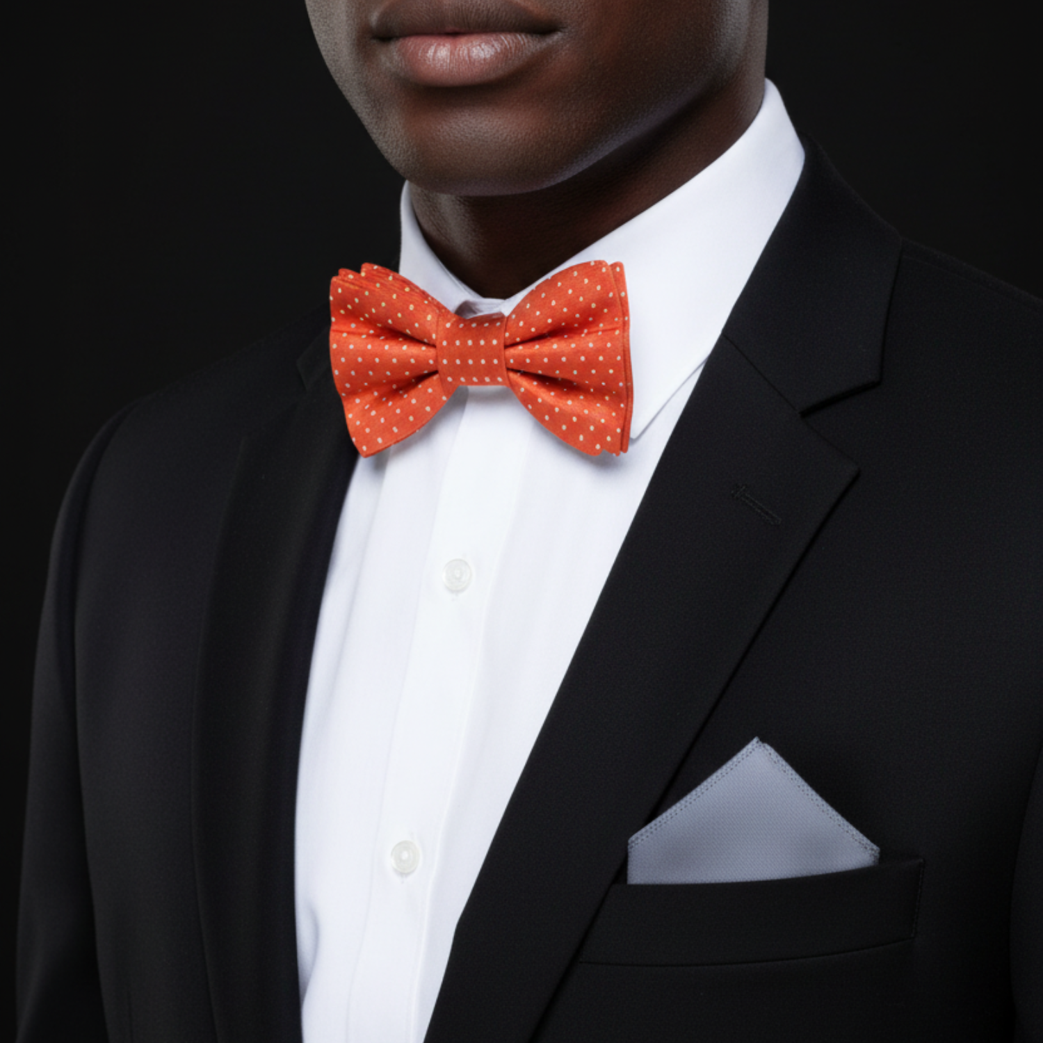 Man wearing a black suit with a white shirt and red polka dot bow tie on a black background