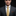 Man wearing a dark suit with a gold tie and pocket square on a black background