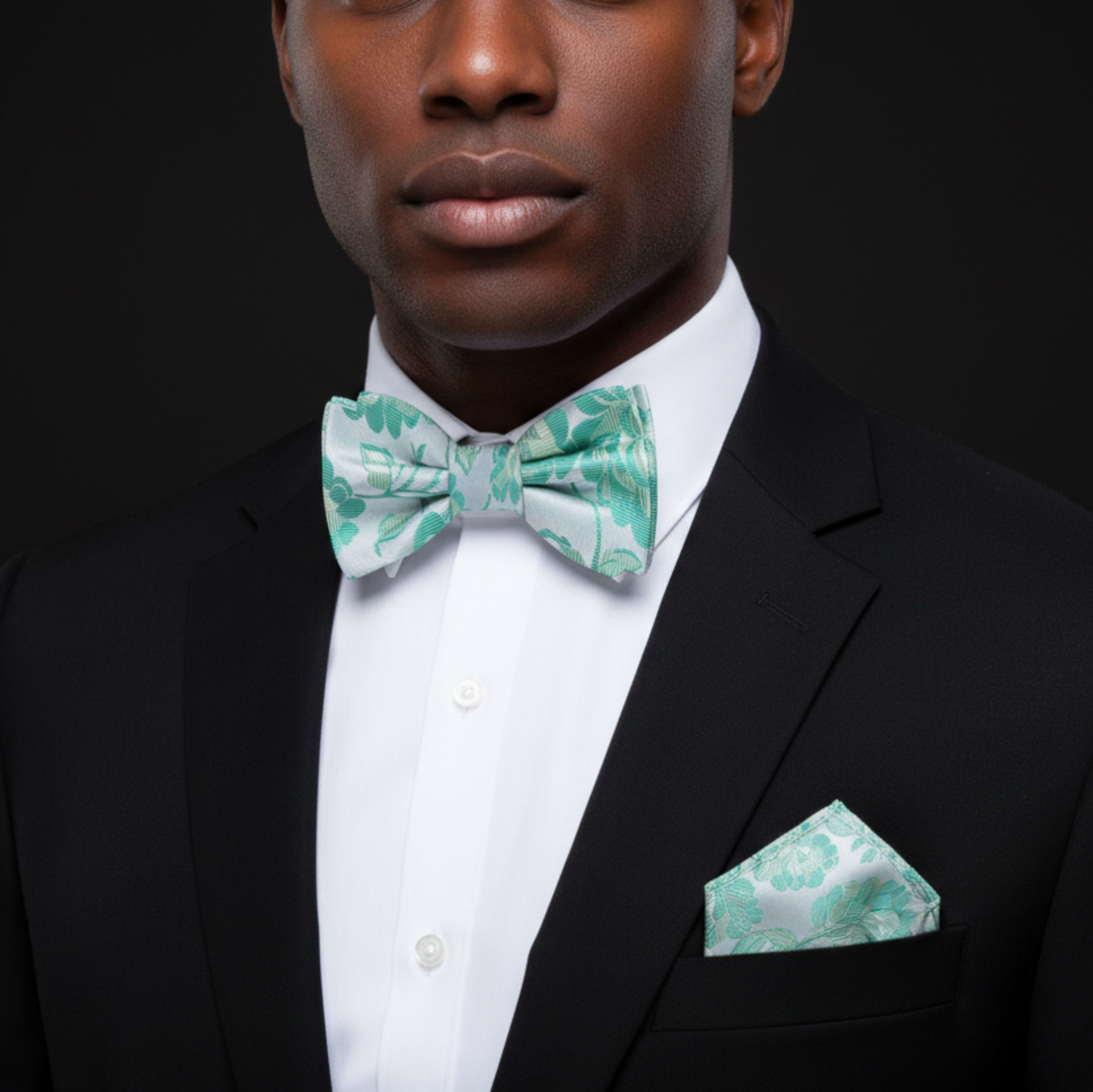 Man wearing a black suit with a white shirt and green bow tie and pocket square on a black background