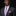 Man wearing a dark suit with a pink and blue checkered tie and pocket square on a black background