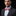 Man wearing a gray suit with a light blue shirt and a red paisley bow tie on a black background