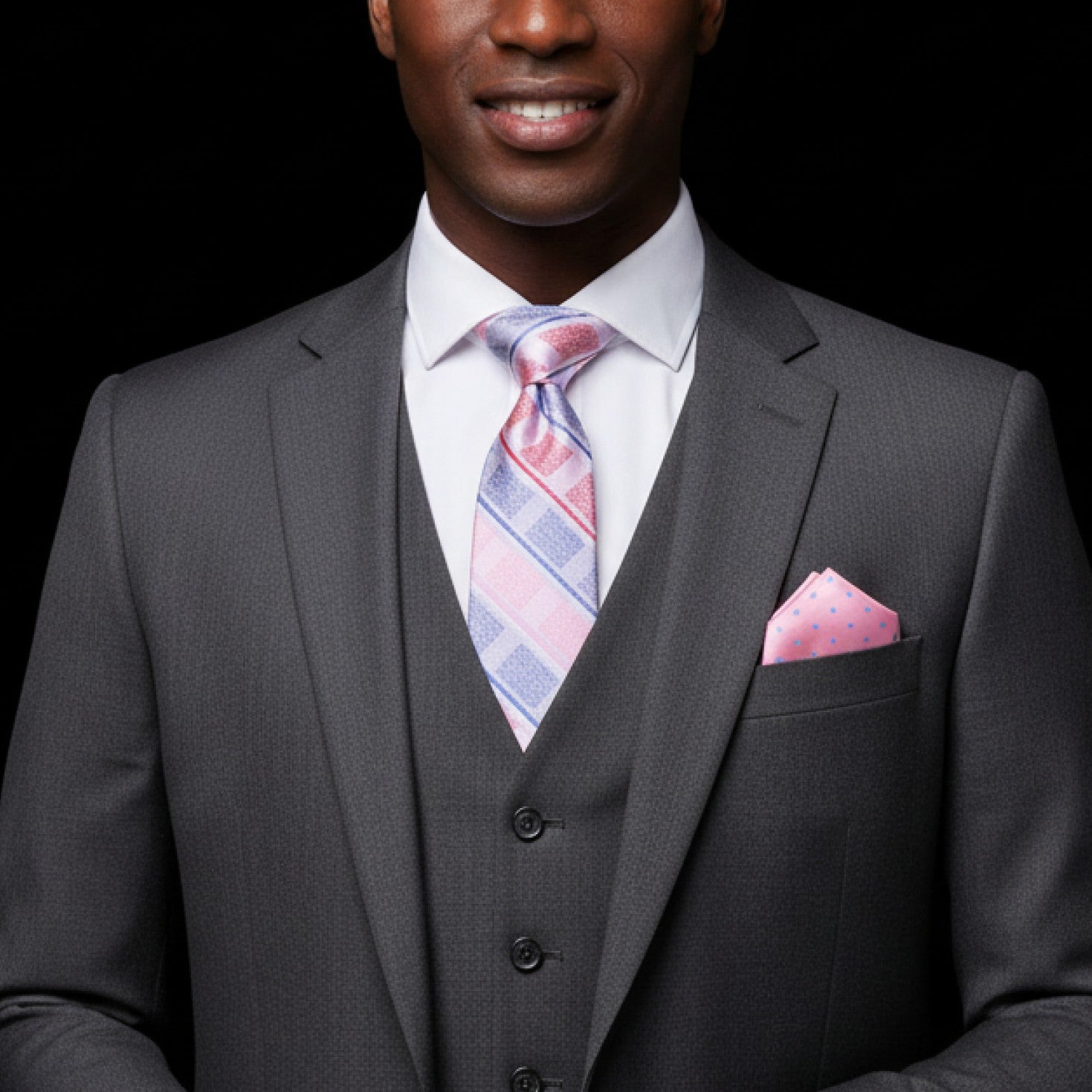 Man wearing a gray suit with a pink and blue striped tie and pocket square on a black background