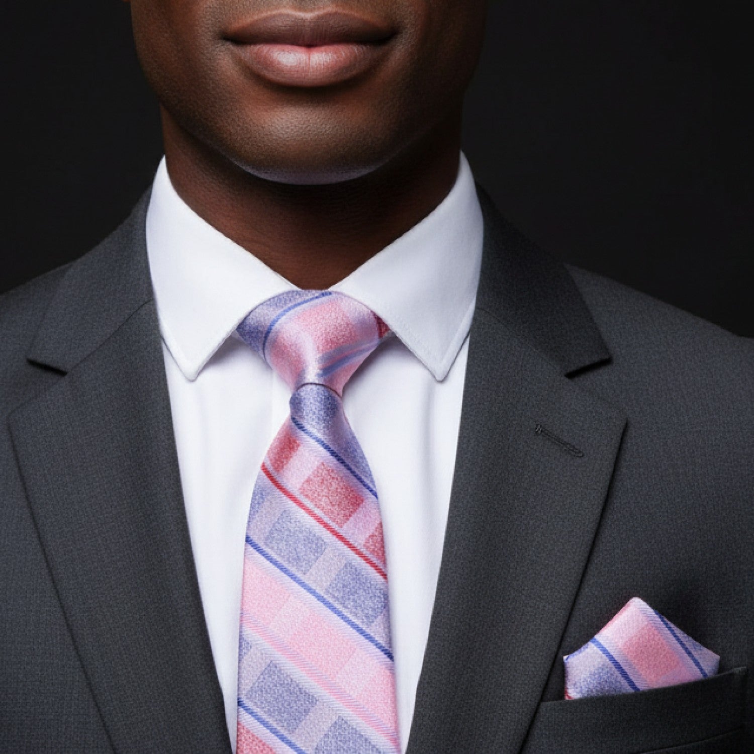 Man wearing a gray suit with a pink and blue striped tie and pocket square on a black background
