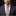 Man wearing a dark suit and patterned tie against a black background