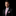 Man wearing a black suit with a pink striped tie and pocket square on a black background