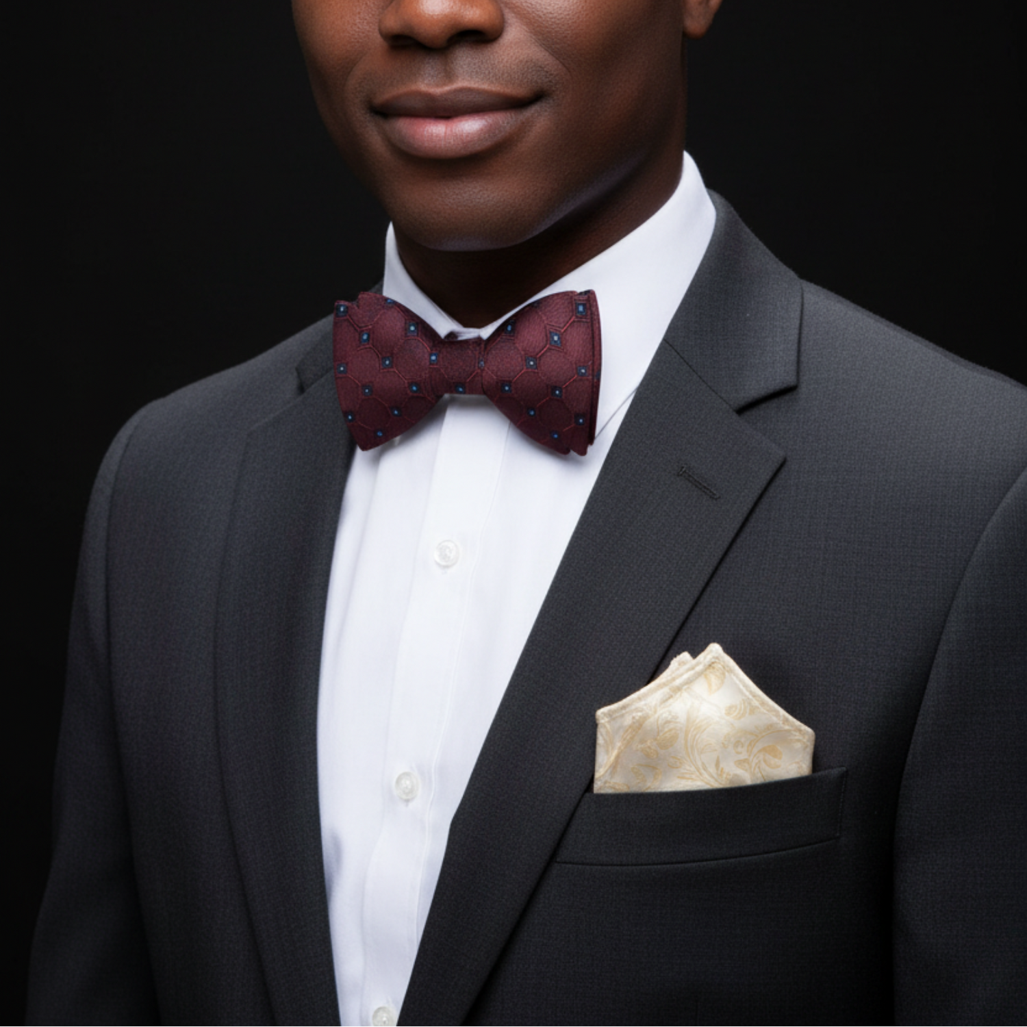 Man wearing a dark suit with a patterned bow tie and pocket square on a black background