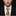 Man wearing a black suit with a white shirt and a gold patterned tie against a black background