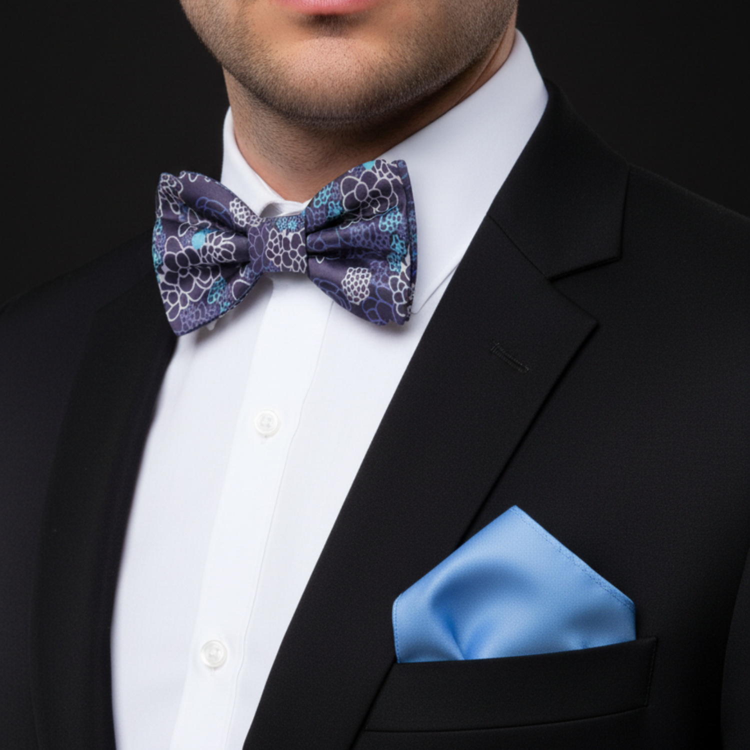 Man wearing a black suit with a patterned purple bow tie and blue pocket square.