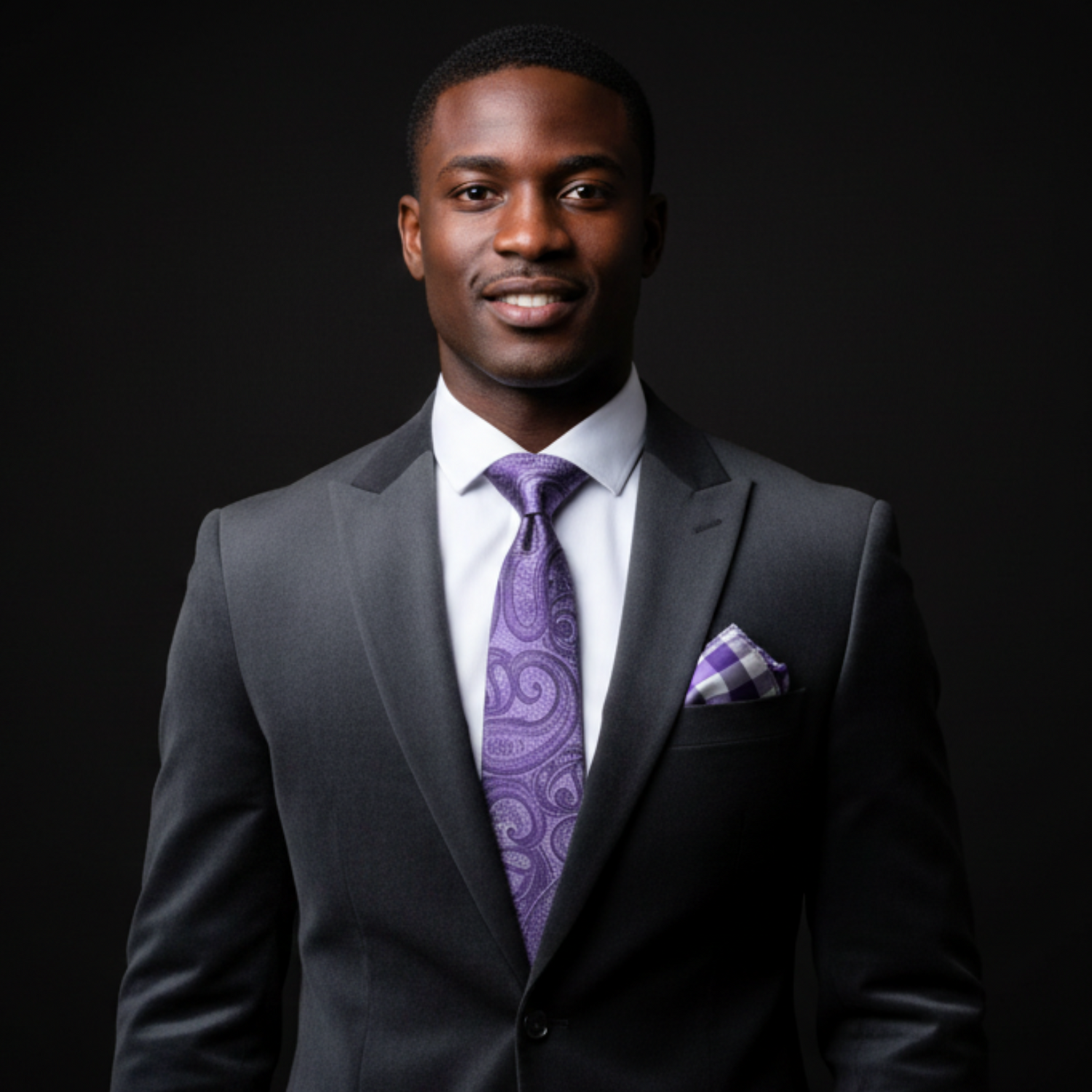Man wearing a gray suit with a purple tie and pocket square on a black background