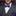 Man wearing a gray suit with a purple paisley bow tie and pocket square in front of a bookshelf.