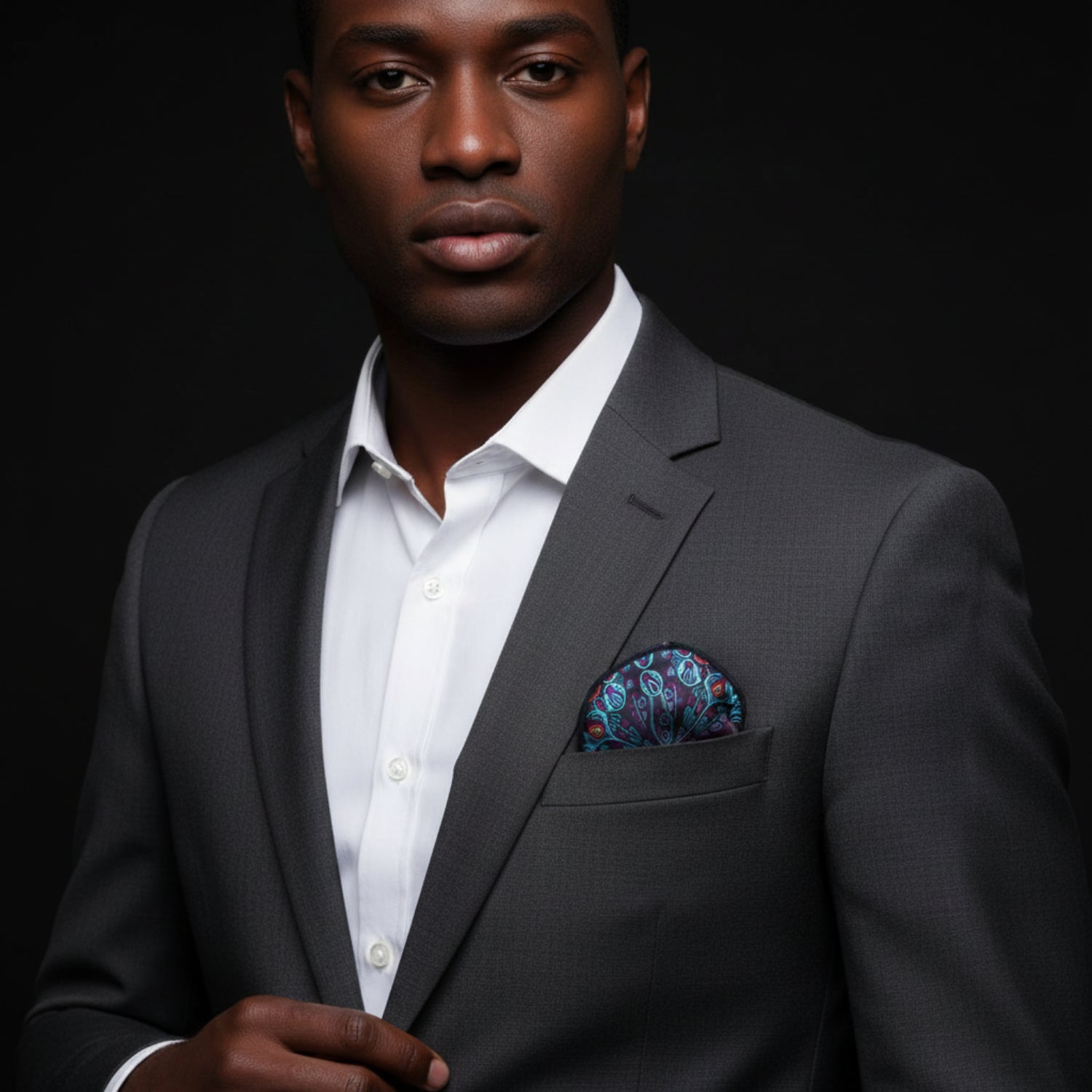 Man wearing a dark suit with a patterned pocket square against a black background
