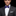 Man wearing a black suit with a white shirt and purple bow tie on a black background
