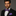 Man wearing a black suit with a purple bow tie and matching pocket square on a gray background