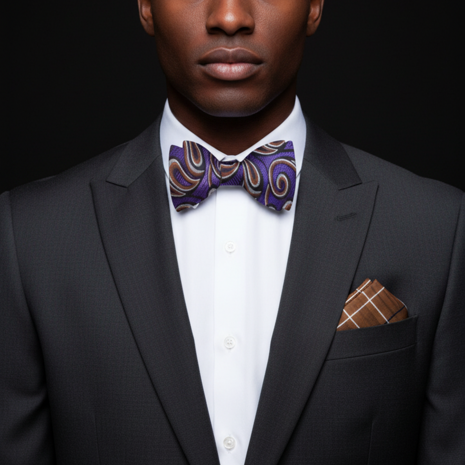 Man wearing a black suit with a purple bow tie and brown pocket square against a dark background