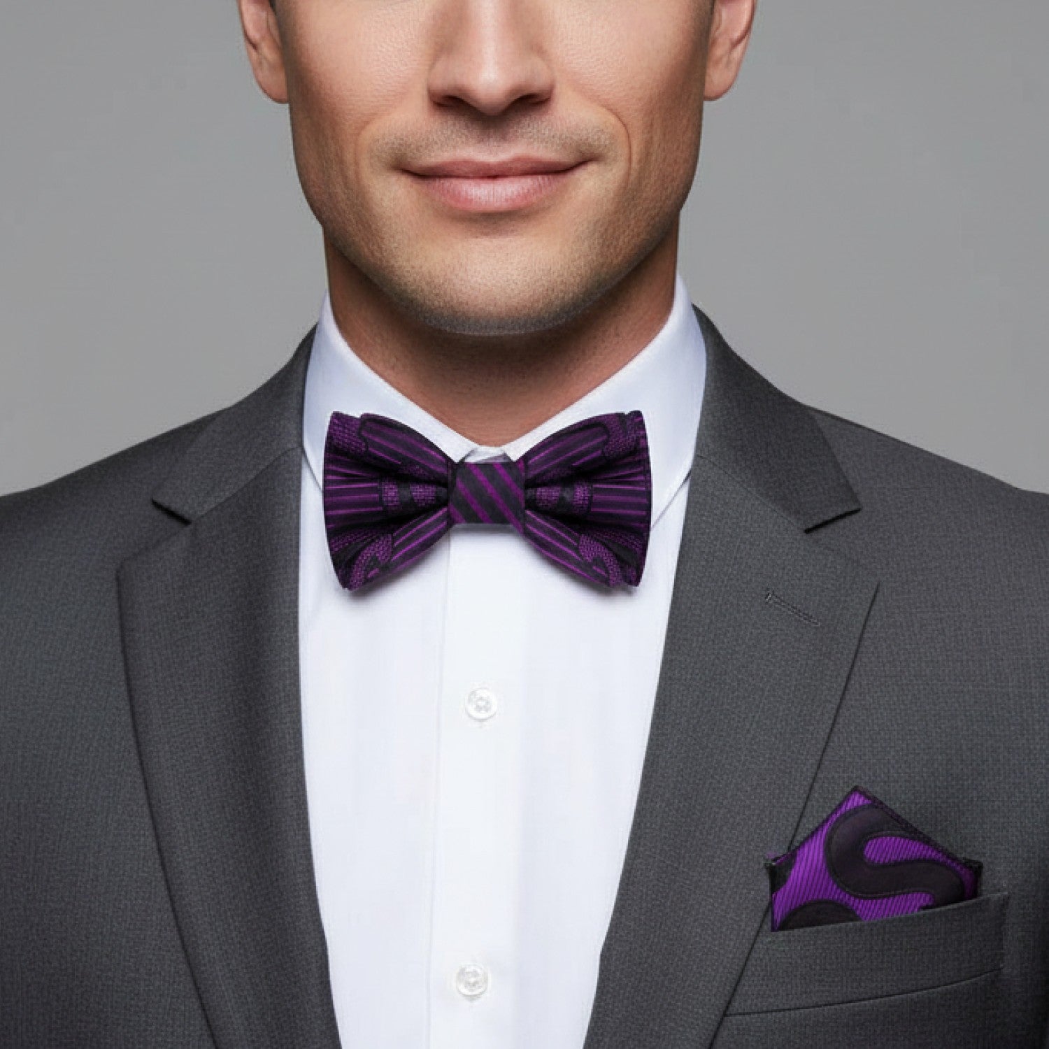 Man wearing a gray suit with a purple bow tie and pocket square on a gray background