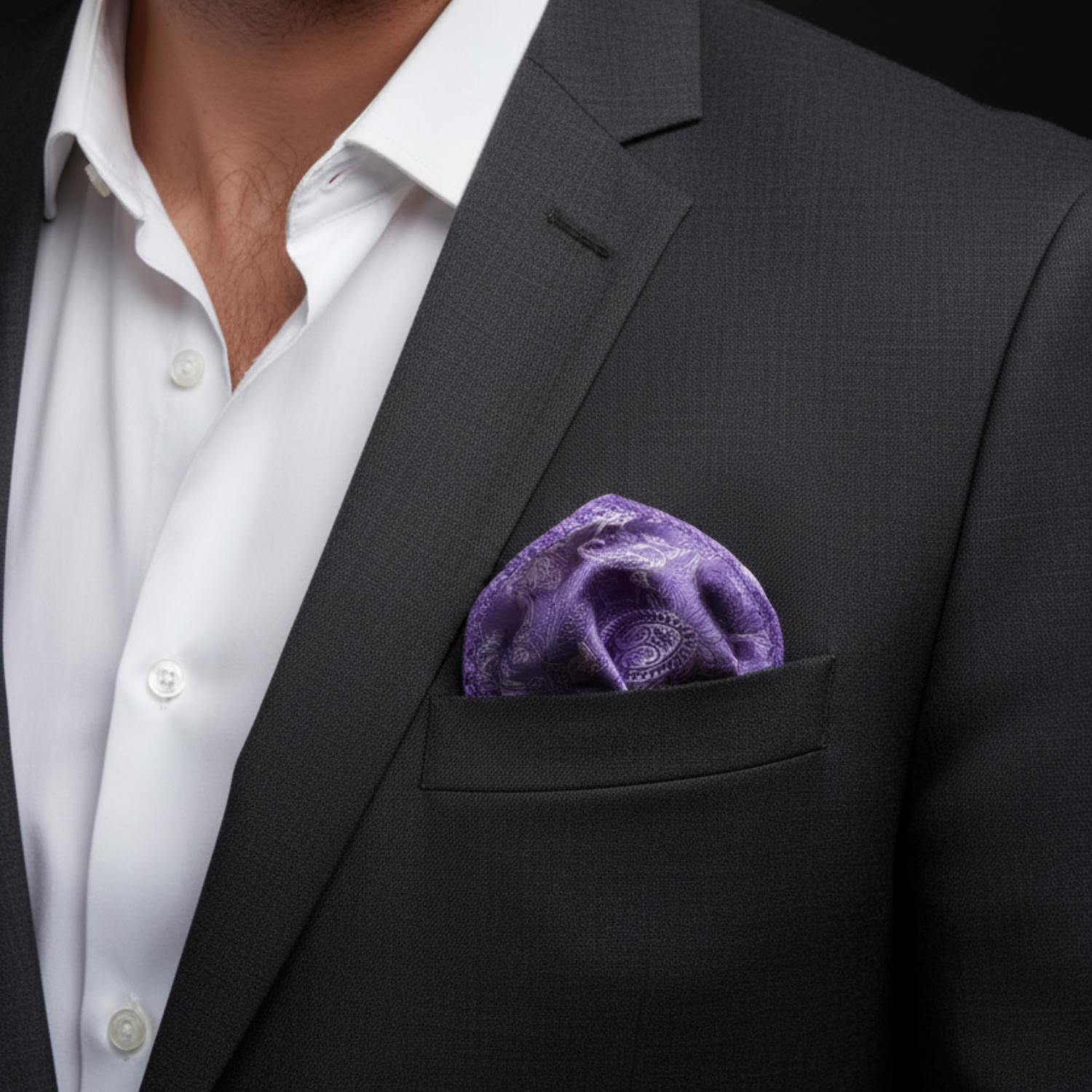Man wearing a black suit with a white shirt and purple pocket square against a dark background
