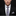 Man wearing a black suit with a plaid tie and pocket square on a dark background