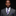 Man wearing a gray suit with a purple and gray checkered tie against a black background
