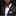 Man wearing a black suit with an orange and black patterned bow tie and pocket square against a black background