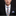 Man wearing a black suit with a colorful checkered tie and pocket square on a dark background
