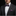 Man wearing a black suit with a white shirt, purple bow tie, and matching pocket square on a black background.