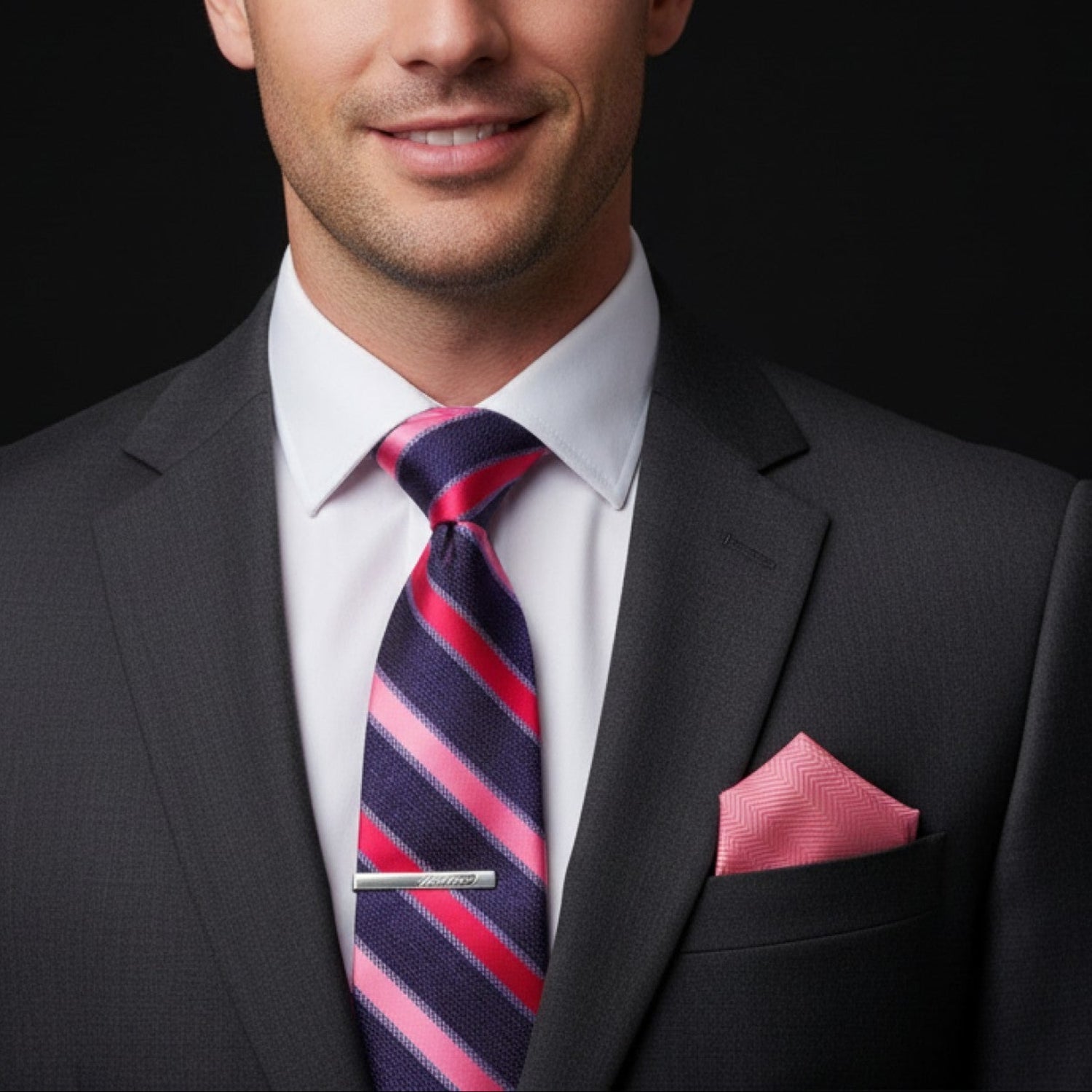 Man wearing a gray suit with a striped tie and pink pocket square on a black background