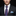 Man wearing a black suit with a purple tie and patterned pocket square on a black background