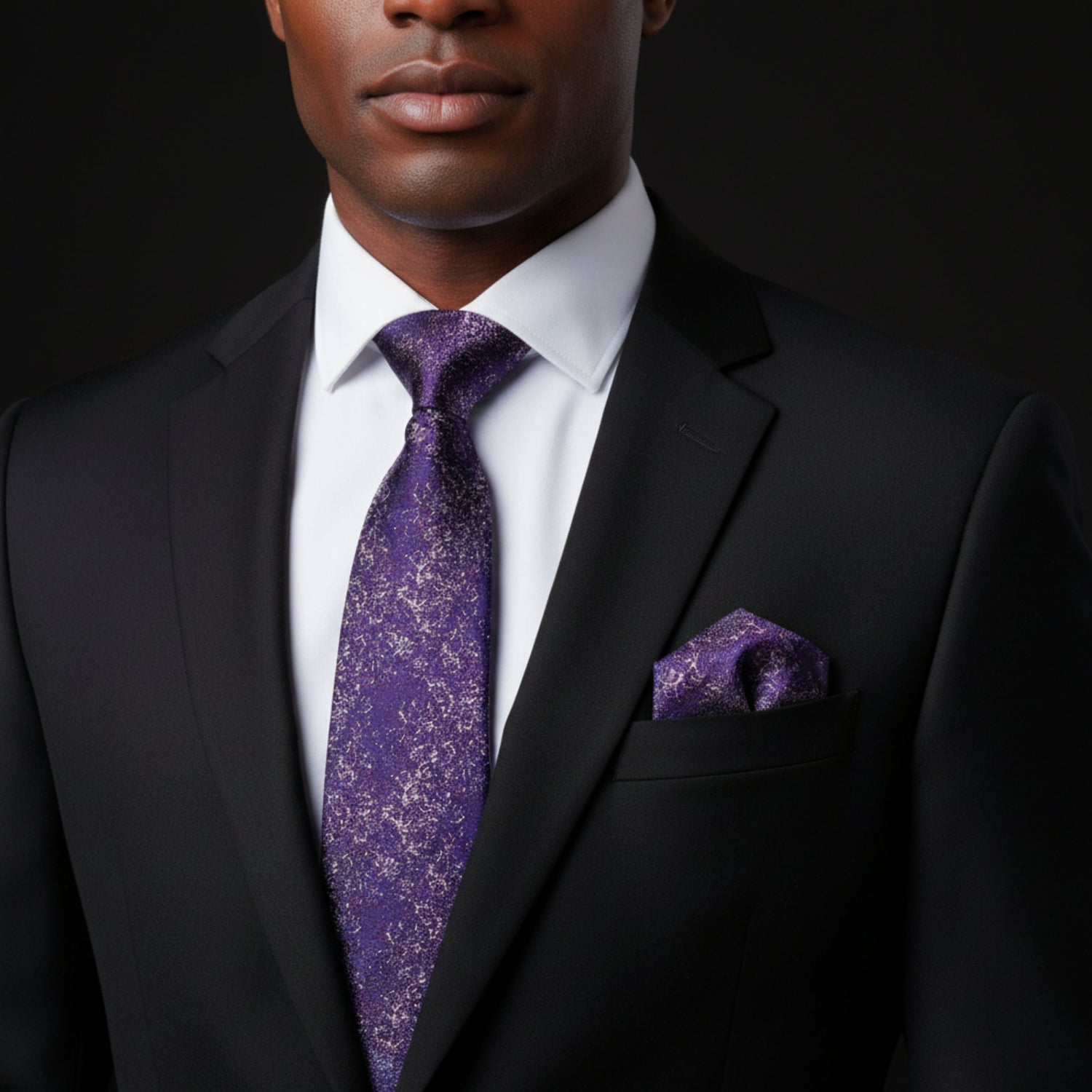 Man wearing a black suit with a purple tie and pocket square on a dark background