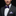 Man wearing a black suit with a purple bow tie and matching pocket square on a dark background
