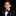 A young boy wearing a black suit jacket, white dress shirt, and a purple paisley bow tie with a matching pocket square, photographed against a solid black background.