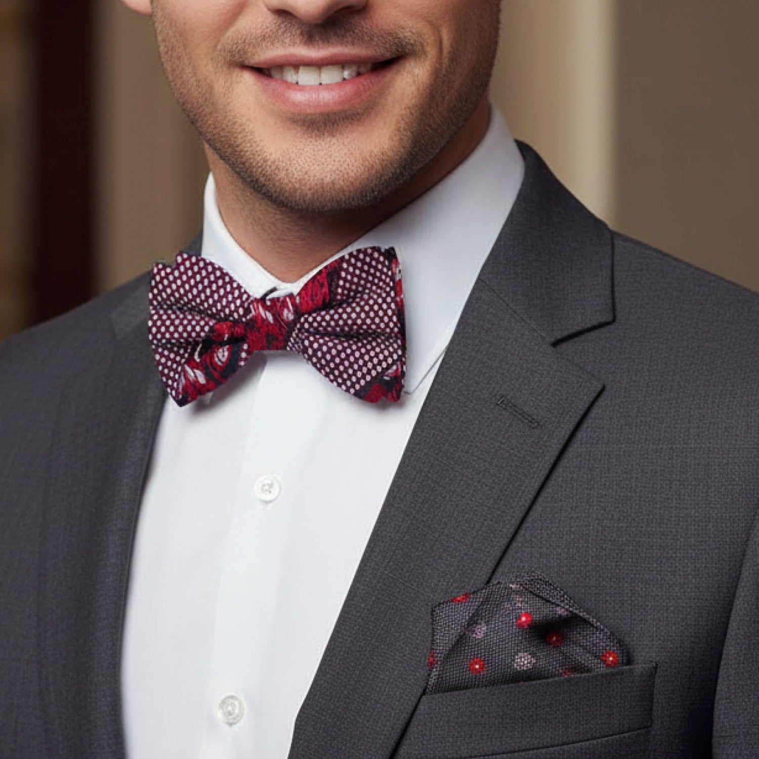 Man wearing a gray suit with a red patterned bow tie and pocket square.