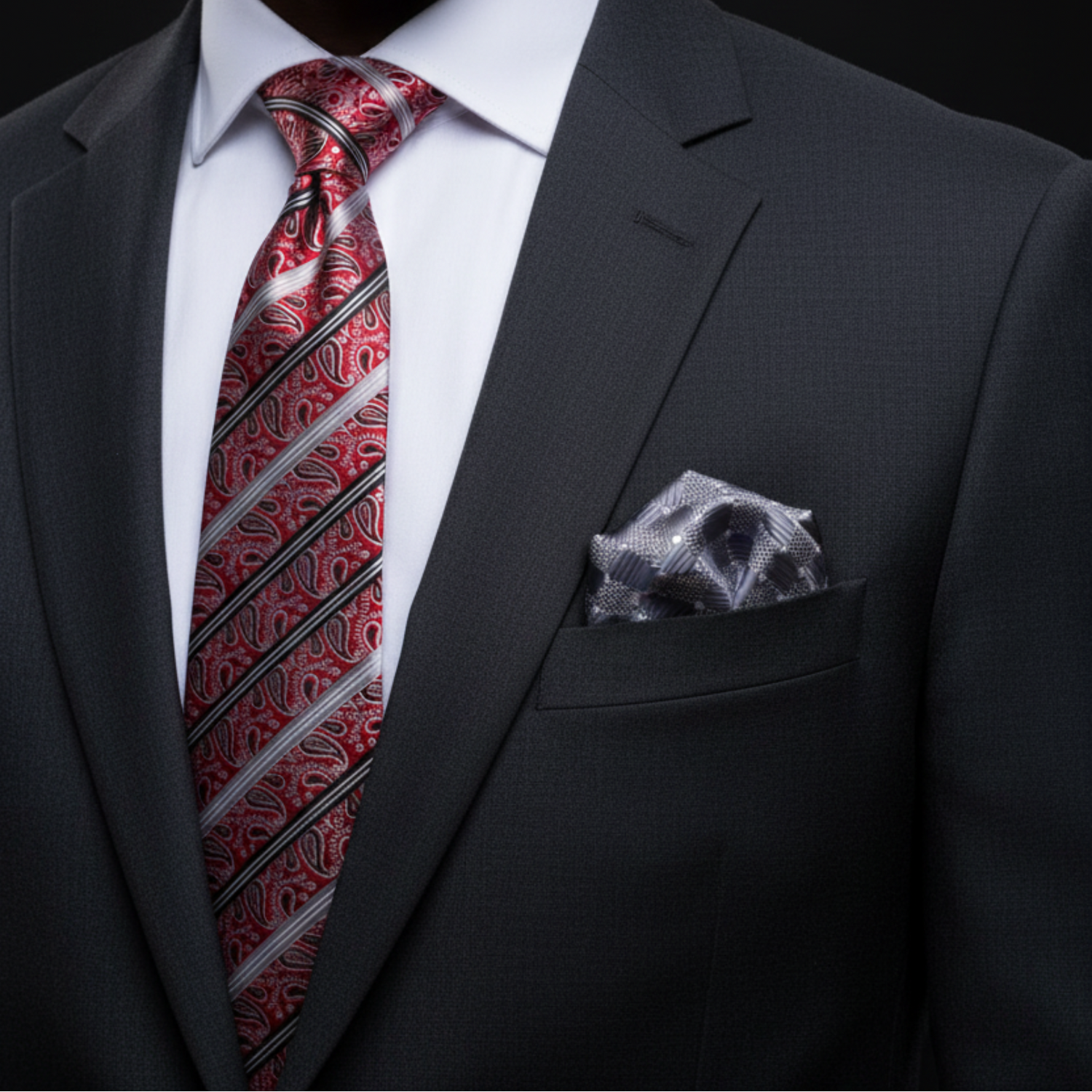 Black suit with a red paisley tie and patterned pocket square on a black background