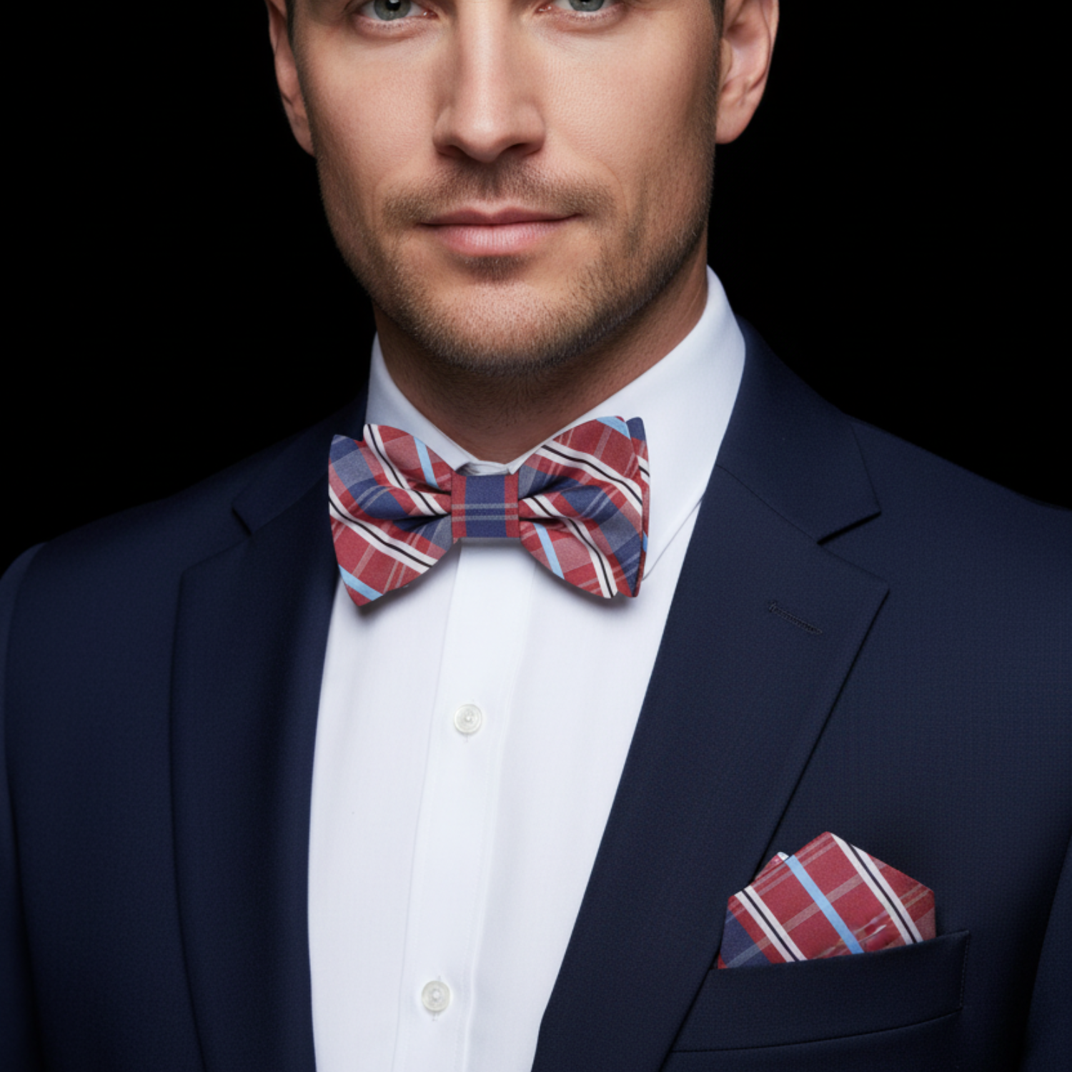 Man wearing a navy suit with a red and blue striped bow tie and pocket square against a black background