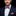 Man wearing a navy suit with a red and blue striped bow tie and pocket square against a black background